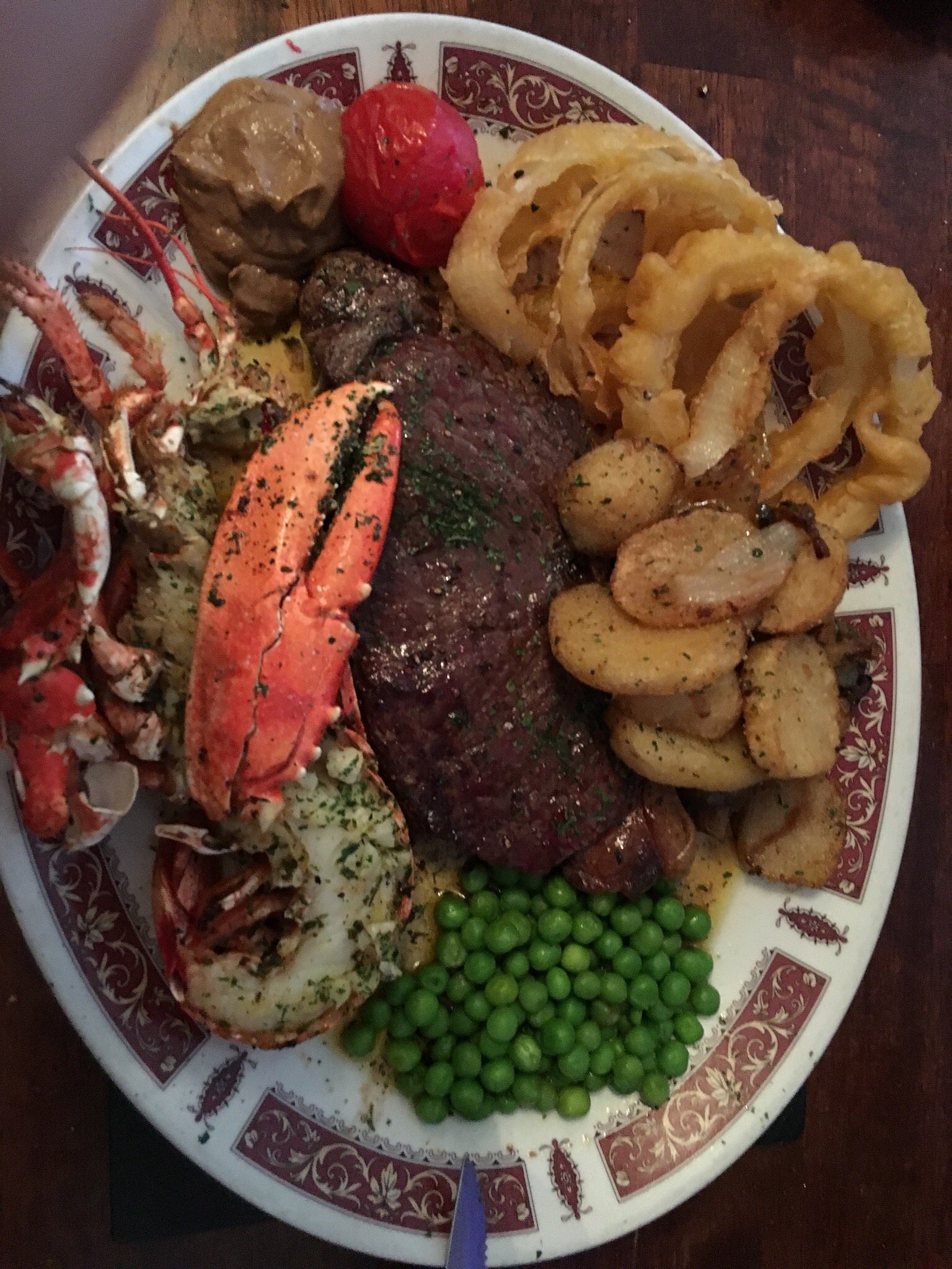 Steak and lobster with onion rings, potatoes and peas